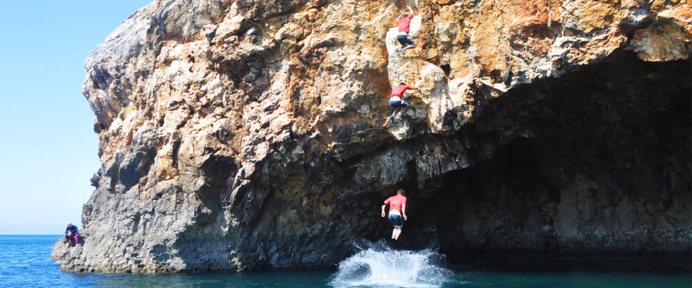 man jumping in water after deep water soloing - rock climbing